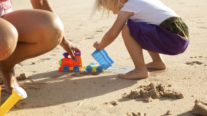Symbolbild: Ein Kind spielt mit Plastikfahrzeugen im Sand eines Strandes, man erkennt das Kind nicht