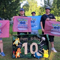 Fünf Menschen stehen mit "Pokemon GO"-Bannern hinter einem "Happy Birthday Pokemon GO"-Plakat.