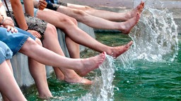 Mehrere Personen baden ihre Füße im Wasser eines Brunnens