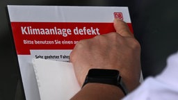 Ein Bahnmitarbeiter hängt einen Informationszettel über eine defekte Klimaanlage auf