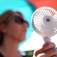Eine Frau kühlt sich mit einem Handventilator unter Sonnenschirmen auf einem Balkon in der Mittagssonne ab