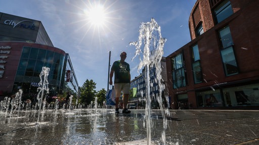 Ein Mann geht bei hohen Temperaturen und strahlendem Sonnenschein durch einen begehbaren Brunnen in der Innenstadt