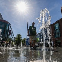 Ein Mann geht bei hohen Temperaturen und strahlendem Sonnenschein durch einen begehbaren Brunnen in der Innenstadt