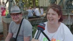 Eine Frau mit roten Haaren und weißem T-Shirt lächelt in die Kamera