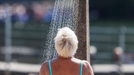 Eine Frau steht zur Abkühlung im Freibad Wolfssee unter der Dusche