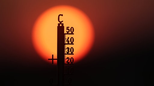 Hinter einem Thermometer geht am Morgen die Sonne auf