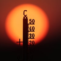 Hinter einem Thermometer geht am Morgen die Sonne auf
