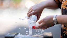 Ein Mann füllt an einem Trinkwasserbrunnen eine Flasche auf.