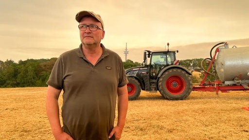 Der Landwirt Markus Wipperfürth steht auf dem Feld vor seinem Traktor.