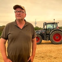 Der Landwirt Markus Wipperfürth steht auf dem Feld vor seinem Traktor.