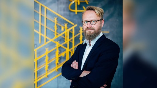 Johannes Wentzel, Medienreferent Münster, steht mit verschränkten Armen vor blauem Hintergrund