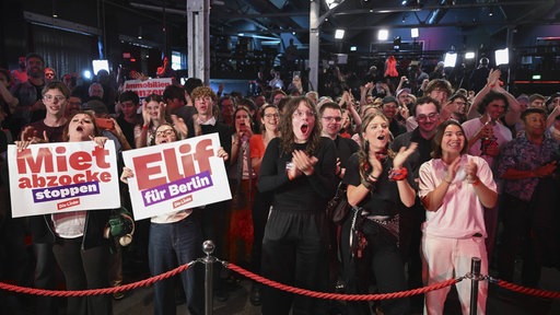 Junge Wähler stehen gemeinsam und feiern die Linke Spitzenkandidatin Elif Eralp. Sie applaudieren und halten Plakate in die Höhe 
