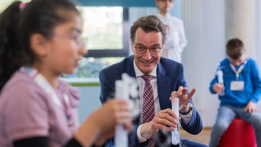 Hendrik Wüst (CDU), Ministerpräsident von Nordrhein-Westfalen, hält ein Reagenzglas in der Hand.