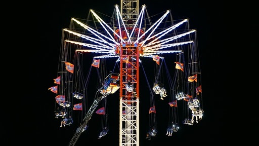 Menschen sitzen im Kettenkarussell am Hamburger Dom fest. Vorne links ist eine Drehleiter der Feuerwehr zu sehen.