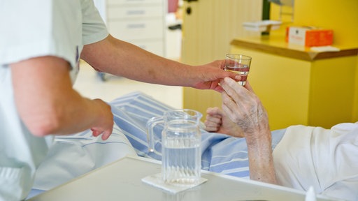 Eine Krankenpflegerin reicht einem Patienten in einem Klinikum ein Glas Wasser