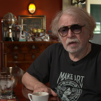 Zirkusdirektor Bernhard Paul trägt eine große Sonnenbrille und sitzt seitlich am Tisch.