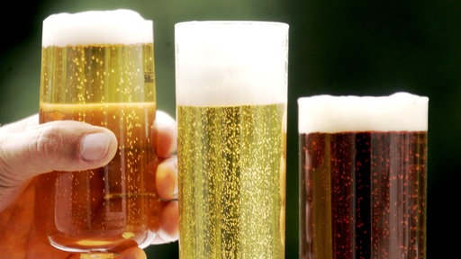 Eine Hand hält ein Bierglas neben verschiedenen weiteren Biersorten