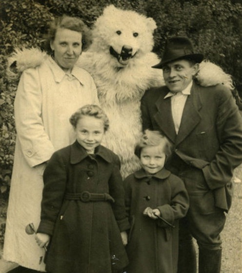 Ein als Eisbär verkleideter Mensch hat den Arm um eine Frau und einen Mann gelegt. Vor ihm stehen zwei Kinder.