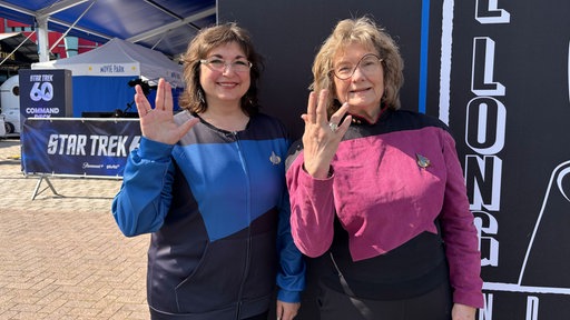 Zwei Frauen in Star-Trek-Uniformen grüßen mit dem vulkanischen Gruß "live long and prosper" in die Kamera. Sie sind Teil eines Fan-Treffens zu 60 Jahren Star Trek