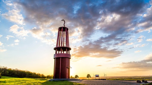 eine große Skulptur in Form einer Lampe vor Sonnenuntergang