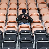 Symbolbild: Ein Fan sitzt auf einer Tribüne im Fußballstadion, deren Plätze ansonsten alle leer sind und liest in einem Buch.