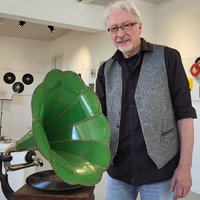 Ein älterer Herr steht neben einem grünen Grammophon