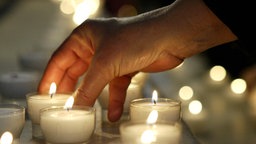 Eine brennende Kerze wird in einer Kirche zwischen andere Kerzen gestellt