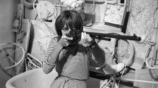Niki de Saint Phalle schießt mit einem Gewehr auf ihr Kunstwerk