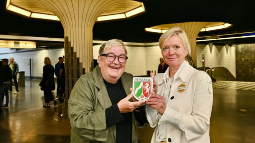 Zwei Frauen mit einer Plakette mit dem Logo des Landes NRW