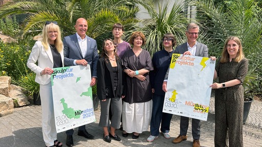 Acht Personen präsentieren zufrieden zwei Skulptur Projekte Plakate.