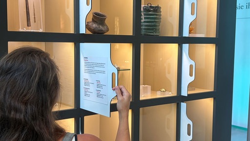 Eine Museumsbesucherin betrachtet in einer Vitrine Ausstellungsstücke.