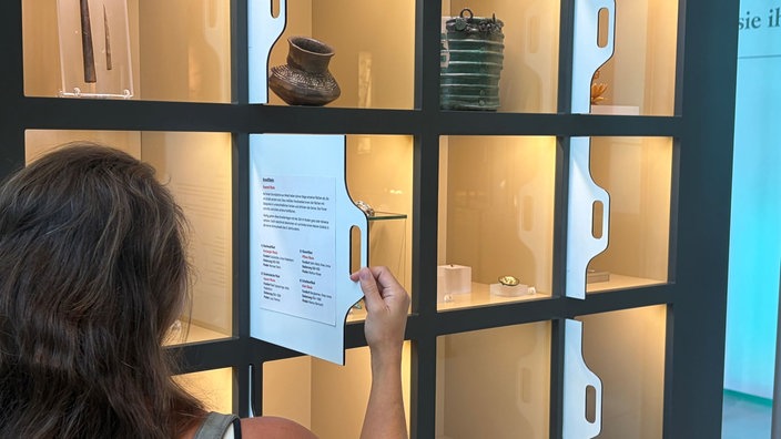 Eine Museumsbesucherin betrachtet in einer Vitrine Ausstellungsstücke.