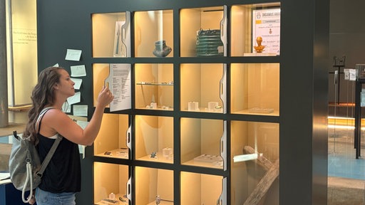 Eine Museumsbesucherin betrachtet in einer Vitrine Ausstellungsstücke.