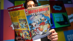 Ein Mann hält eine Jubiläumsausgabe des Micky Maus Magazins in den Händen.