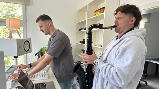 Zwei Männer produzieren Musik am Rechner, einer spielt Saxofon