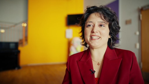 Porträtaufnahme von Pamela Banchetti im roten Anzug vor orangefarbener Wand.