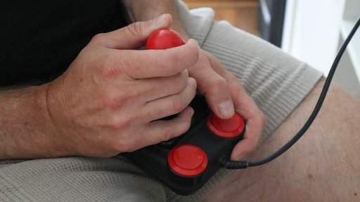 Eine Hand steuert einen roten Joystick. Der Joystick gehört zum Commodore Amiga 500, einem legendären Heimcomputer aus dem Jahr 1987.