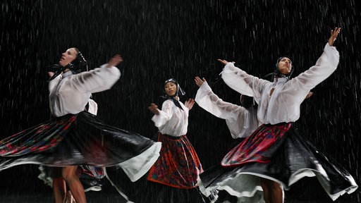 Tänzerinnen in Tracht auf einer dunklen Bühne