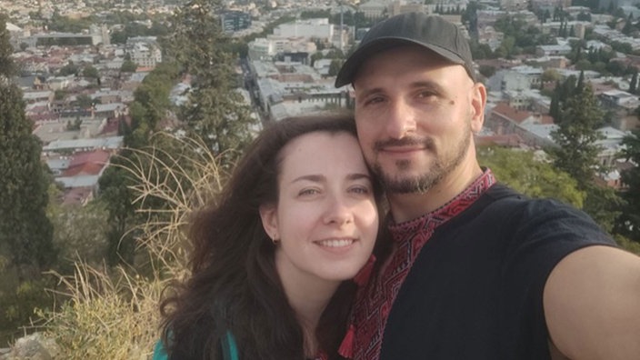 Ein Mann und eine Frau machen zusammen ein Selfie, hinter ihnen ist eine Stadt zu sehen.