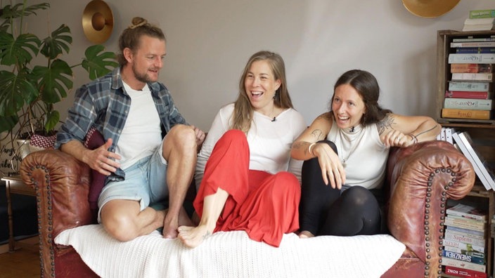Ein Mann und zwei Frauen sitzen zusammen auf einem Sofa und lachen