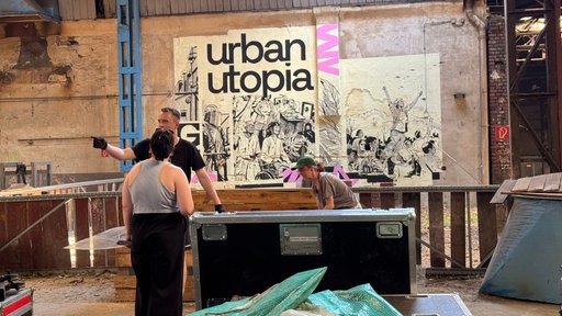 Menschen stehen in einer alten Industriehalle und bauen das Festival auf.