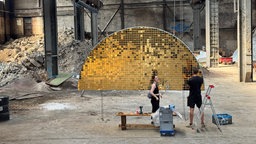 Ein goldenes halbrundes Kunstwerk steht in einer alten Industriehalle.