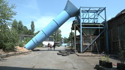 Blaues Gerüst steht neben einem alten Gebäude. Daneben liegt ein blauer Schornstein.