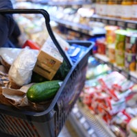 Eine Person trägt einen gefüllten Einkaufskorb durch einen Supermarkt