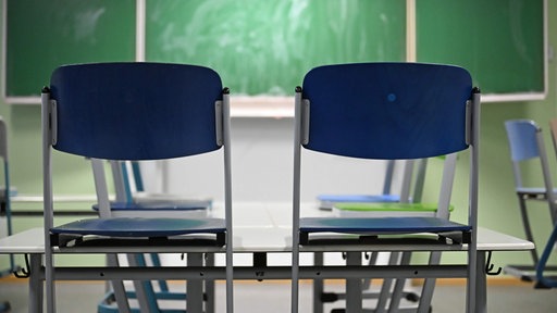 Zwei leere Stühle stehen in einem Klassenraum vor einer Tafel