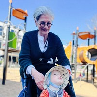 Ein Spielplatz. Katrin Hesse steht hinter einem Kinderwagen. Darin sitzt Philipp. Sie lächelt.