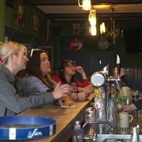 Frauen sitzen an einer Theke, ein Mann zapft dahinter ein Bier.