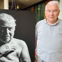 Ernst Sprick steht neben einem Schwarz-Weiß-Porträt von ihm, auf dem seine Brustkrebs-Narbe zu sehen ist