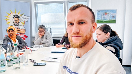 Ylber Uka sitzt im Vordergrund an einem Tisch mit weiteren Schülern und Schülerinnen im Klassenraum
