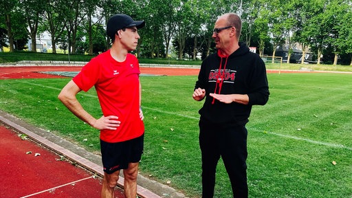 Sebastian Schmitz und sein trainer Guido Kluth stehen nebeneinander auf dem Trainingsplatz und reden miteinander.
